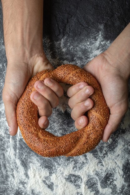 Vertikales Foto von Frauenhänden, die frischen türkischen Simit halten.