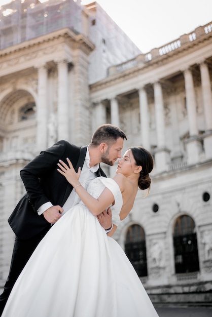 Vertikales Hochzeitsfoto von Bräutigam und Braut einen Moment vor einem Kuss vor dem historischen Gebäude