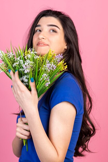 Vertikales Porträt des jungen Mädchens umarmte ihre Blumen und stand auf rosa Hintergrund Hochwertiges Foto