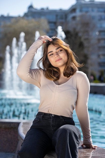 Vertikales Porträt einer jungen Dame, die im Park neben einem Brunnen sitzt Foto in hoher Qualität