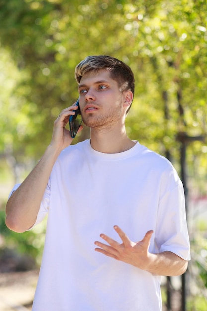 Vertikales Porträt eines jungen gutaussehenden Mannes, der ein T-Shirt trägt und am Telefon spricht Foto in hoher Qualität