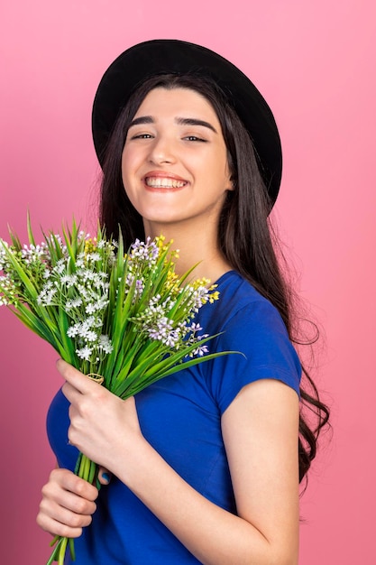 Vertikales Porträt eines jungen Mädchens, das frische Blumen hält und lächelt Hochwertiges Foto