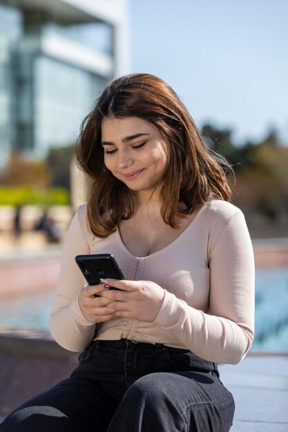 Vertikales Porträt eines jungen schönen Mädchens, das auf ihr Telefon schaut und lächelt Hochwertiges Foto