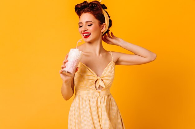 Verträumtes attraktives Mädchen, das Milchshake trinkt. Romantische Ingwerfrau, die Getränk auf gelbem Raum genießt.