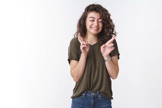 Verträumtes süßes glückliches junges Mädchen, das betet, glaube, Wunder schließen die Augen, die breit die Finger kreuzen, während sie den Wunsch machen, Gott zu bitten, hoffentlich den Traum zu erfüllen, der auf weißem Hintergrund steht und treu erwartet