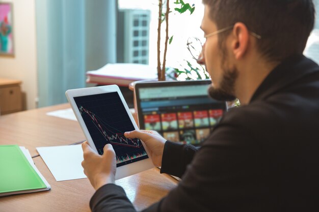 Verwenden von Geräten. Kaukasischer Unternehmer, Geschäftsmann, Manager, der im Büro konzentriert arbeitet. Sieht ernst und beschäftigt aus und trägt klassische Kleidung. Konzept der Arbeit, Finanzen, Geschäft, Erfolg, Führung.