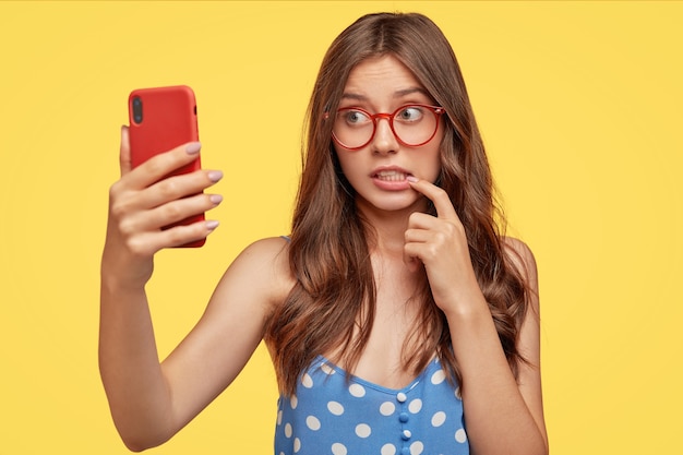 Verwirrte europäische Frau beißt Zeigefinger, macht Selfie-Porträt von elektronischen Gadget