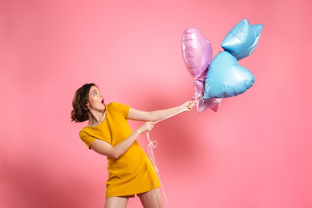 Verwirrte junge Frau im gelben Kleid, das Ballons hält