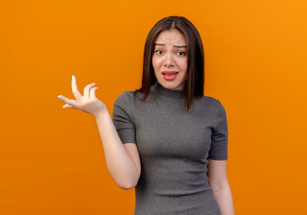 verwirrte junge hübsche Frau, die Hand in der Luft lokalisiert auf Orange mit Kopienraum hält