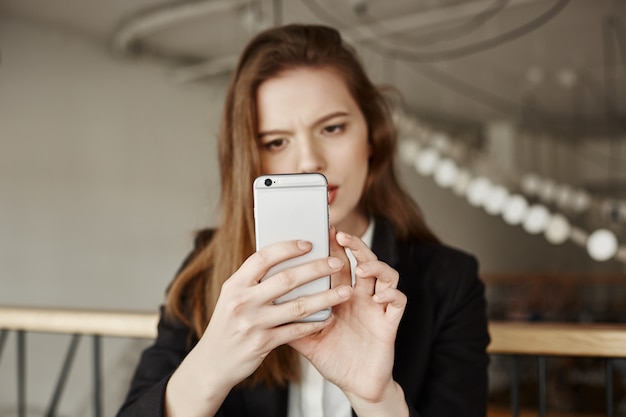 Verwirrte nachdenkliche Frau, die online mit Handy-App einkauft