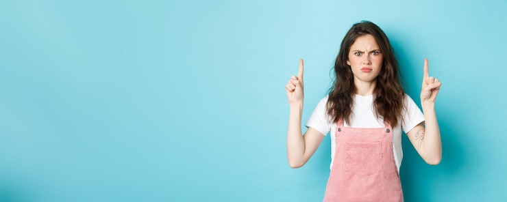 Kostenlose Foto verwirrte und schockierte junge frau runzelt die stirn und starrt unzufrieden auf die nachfrage der kamera, die mit dem finger zeigt