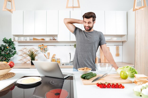 Verwirrter gutaussehender Mann, der Gemüsesalat in der Küche kocht