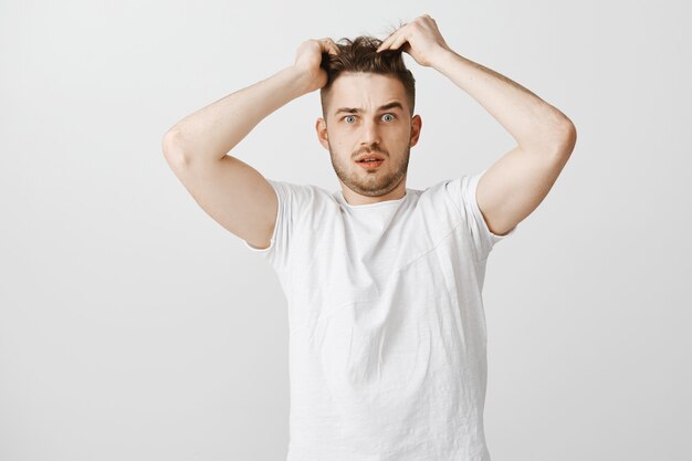Verwirrter junger Mann, der Haare berührt, braucht neuen Haarschnitt