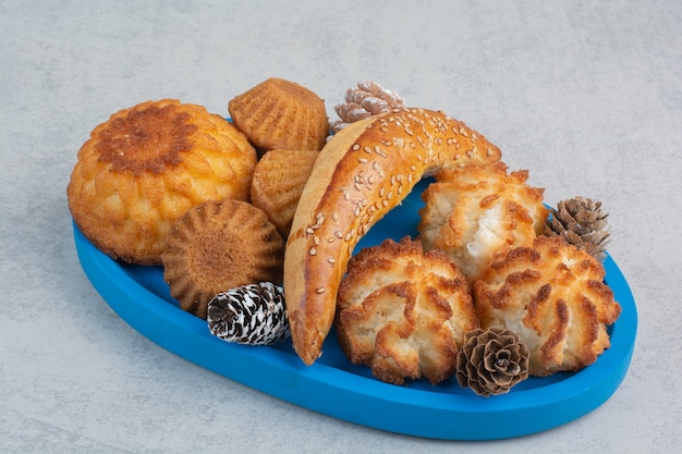 Viele frische leckere Kekse mit kleinen Tannenzapfen auf blauem Teller.