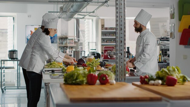 Vielfältiges Team von Köchen, die Bio-Zutaten für die Küche zubereiten und köstliche Gourmet-Mahlzeiten mit Salat und Gemüse in der professionellen Küche zubereiten. Mann und Frau kochen Essen. Stativaufnahme.