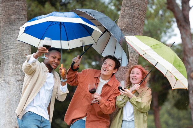 Vier Freunde trinken Wein und stehen während einer Party im Freien unter Regenschirmen