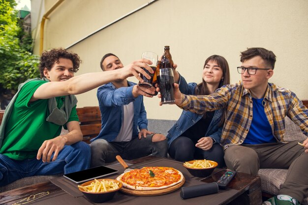 Vier junge Leute, sportliche Fans treffen sich in der Bar. Konzept der Freundschaft, Freizeitbeschäftigung