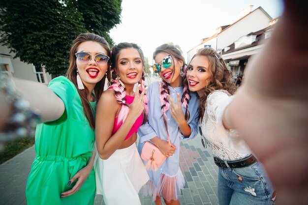 Vier modische und schöne beste Freundinnen in Brillen posieren allgemein für den Lebensstil in sozialen Netzwerken selbst Zeit verbringen Frauen in Sonnenbrillen nach dem Einkaufen und Schönheitssalon
