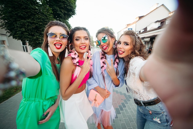 Vier modische und schöne beste freundinnen mit brille, die sich allgemein für soziale netzwerke, lifestyle und zeitvergnügen posieren. frauen in sonnenbrillen nach dem einkaufen und schönheitssalon.