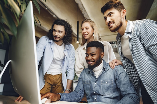 Vier multiethnische Kollegen, die im Büro auf den Computerbildschirm schauen