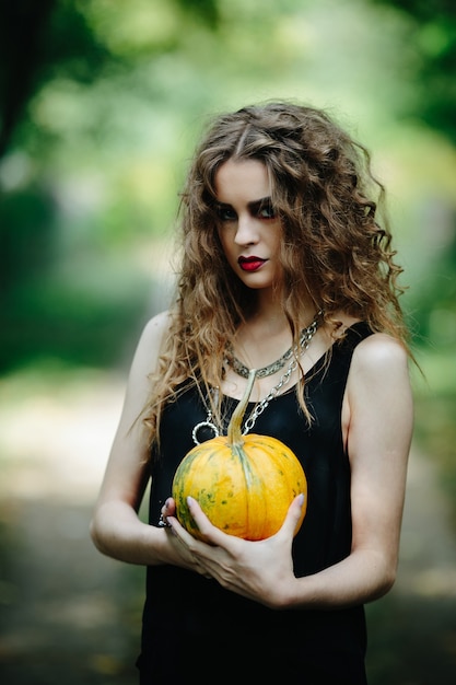 Vintage Frau als Hexe, die am Vorabend von Halloween gegen einen verlassenen Ort posiert