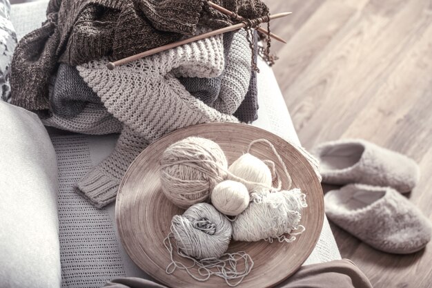 Vintage Holzstricknadeln und -fäden auf einem gemütlichen Sofa mit Kissen und Hausschuhen in der Nähe