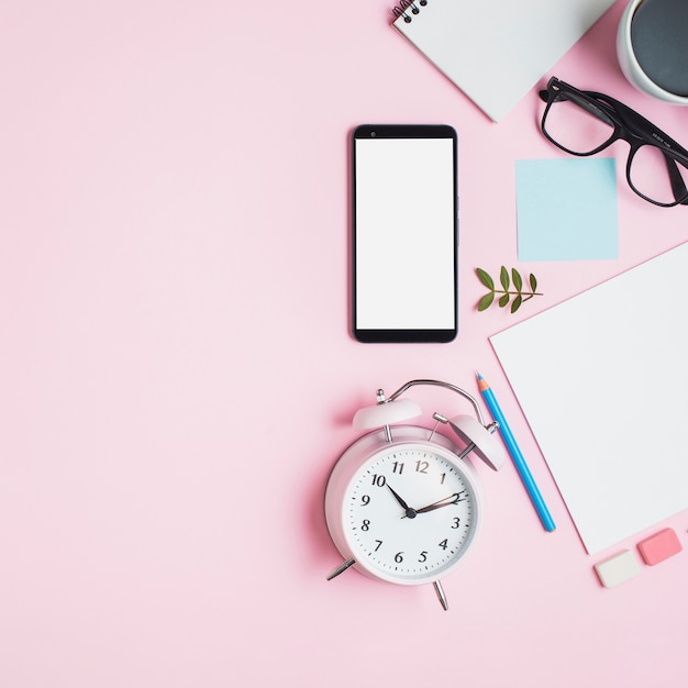 Vintage Wecker; Smartphone; Brillen und Briefpapier auf rosa Hintergrund