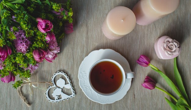 Violette Tulpen, rosa Duftkerzen und eine Tasse Tee