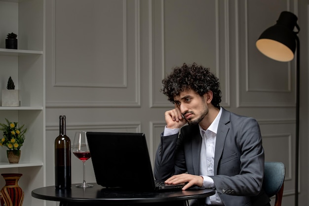 Virtuelle Liebe, hübscher Kerl im Anzug mit Wein auf Ferncomputer-Date, der mit der Hand am Kinn denkt