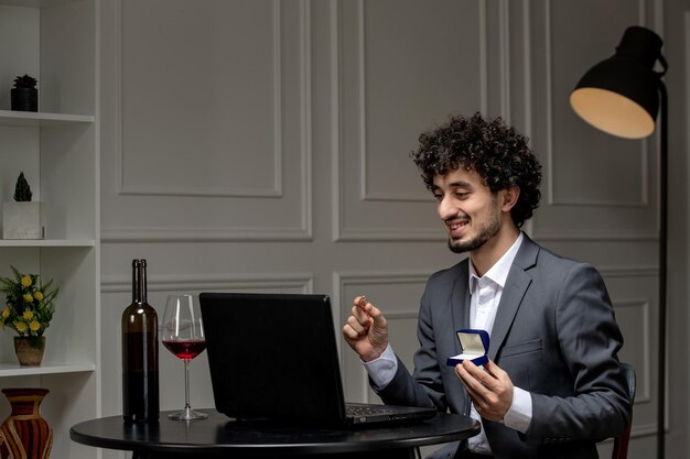 Virtuelle Liebe, hübscher, süßer Kerl im Anzug mit Wein auf einem Distanz-Computer-Date-Holding-Ring in Box