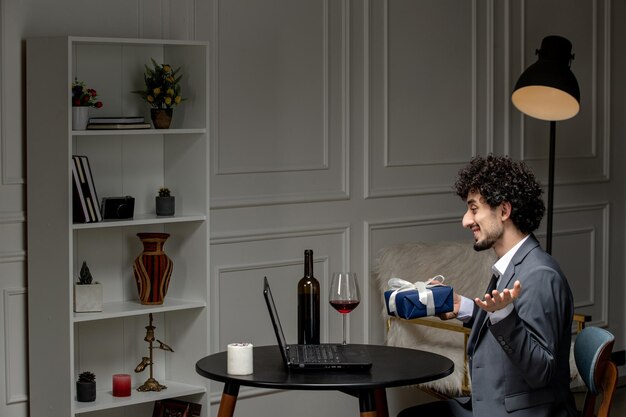 Virtuelle Liebe hübscher süßer Kerl im Anzug mit Wein auf einem Ferncomputerdatum mit Geschenkbox