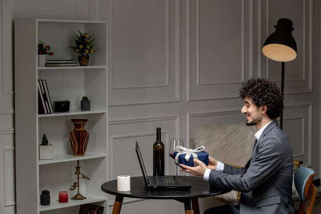 Virtuelle Liebe, hübscher, süßer Kerl im Anzug mit Wein bei einem Ferncomputer-Date, der ein Geschenk gibt