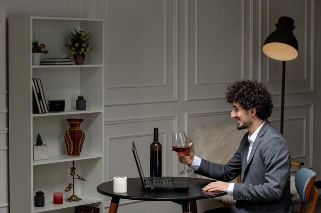 Virtuelle Liebe, hübscher, süßer Kerlanzug mit Wein auf einem Ferncomputerdatum, das Wein aus Glas trinkt