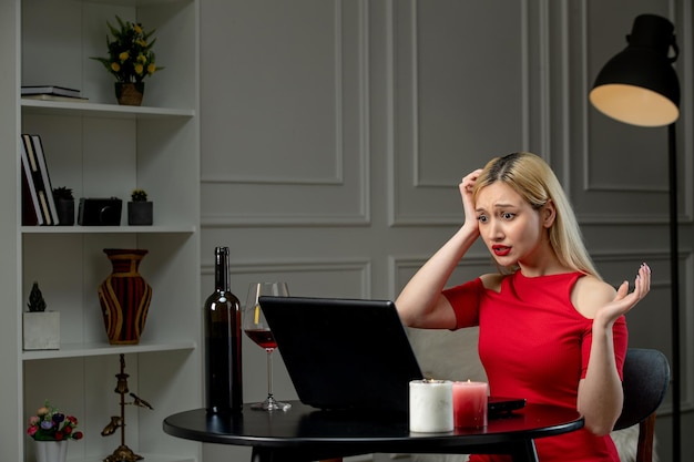 Virtuelle Liebe, süßes blondes Mädchen in rotem Kleid am Ferndatum mit Wein, der den Kopf hält