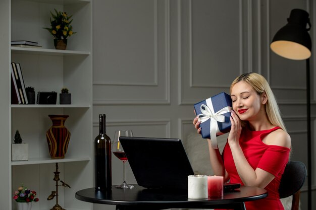 Virtuelle Liebe süßes blondes Mädchen in rotem Kleid am Ferndatum mit Wein geschlossenen Augen mit Geschenkbox
