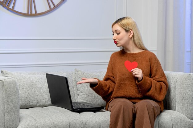 Virtuelle Liebe, süßes junges blondes Mädchen im kuscheligen Pullover auf Ferncomputer-Date, das Küsse sendet