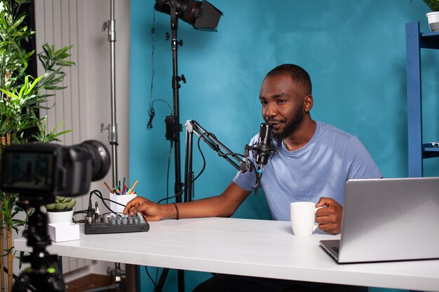 Vlogger passt Lautstärke auf Mischpult an und spricht mit Followern in Online-Morgenshow vor Live-Vlog-Setup. Lächelnder Social-Media-Influencer, der mit dem Publikum interagiert, das am Schreibtisch im Studio sitzt.