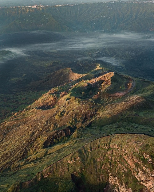 Vogelperspektive auf Hügel, die unter dem Sonnenlicht mit Grün und Nebel bedeckt sind - perfekt für Tapeten