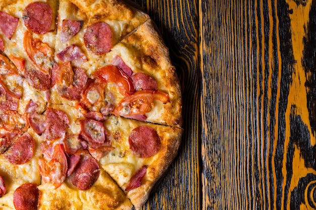 Vogelperspektive blick auf die hälfte der leckeren pizza mit schinken, peperoni, tomaten und sauce auf holztisch Premium Fotos