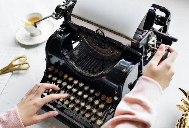 Vogelperspektive einer Frau, die auf einem Retro- Schreibmaschinenleeren papier schreibt