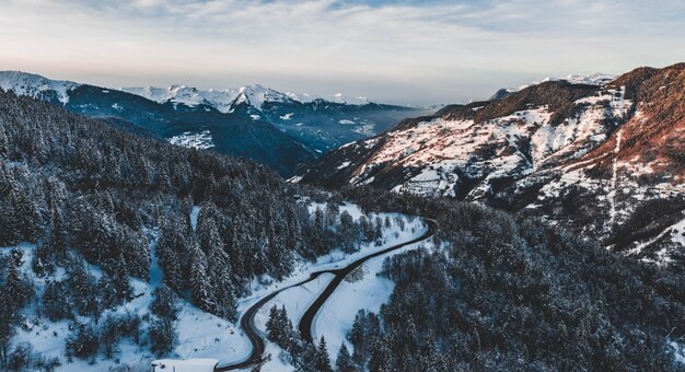 Vogelperspektive einer Straße, die durch schneebedeckte Berge geht, die in einem Kiefernwald bedeckt sind