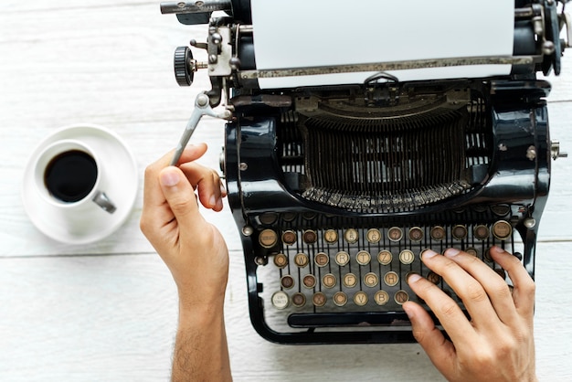Vogelperspektive eines Mannes, der auf einem Retro- Schreibmaschinenleeren papier schreibt