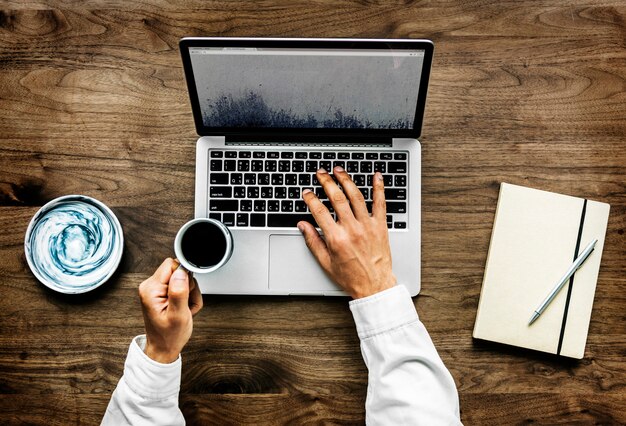 Vogelperspektive eines Mannes, der Computerlaptop auf Holztisch verwendet