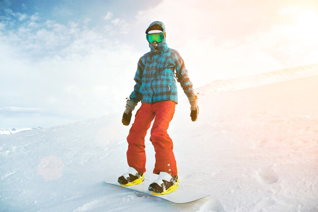 Voll ausgestattet und von einem kalten Anfänger bedeckt, trägt der Snowboarder eine Schneebrille und posiert auf dem Gipfel des Berges