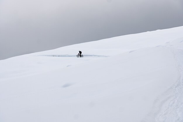 Voll ausgestatteter Radfahrer, der in verschneiten Bergen Fahrrad fährt