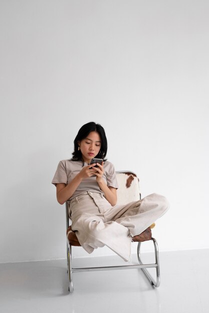 Vollbildfrau auf Stuhl mit Smartphone