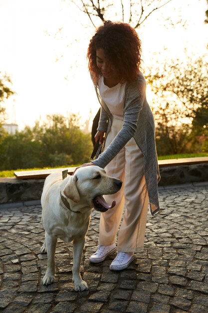 Volle Länge Aufnahme der hübschen gesunden jungen Dame, die am Morgen im Park mit Hund geht