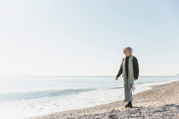 Kostenloses Foto volle schuss alte frau, die am meer geht