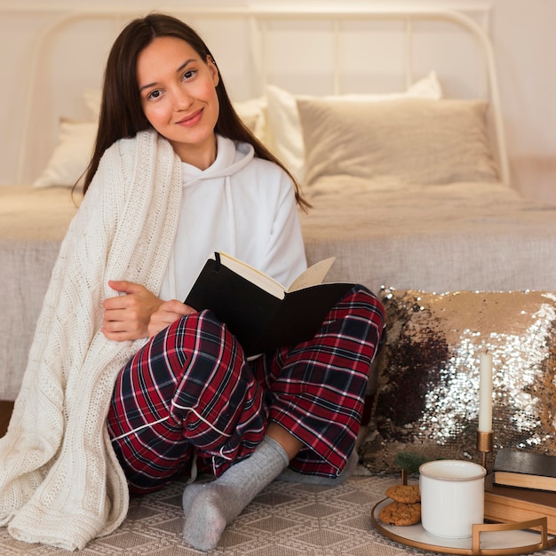 Kostenloses Foto volle schuss schöne frau, die auf teppich mit buch sitzt