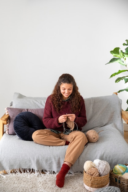 Volle Schussfrau, die auf Couch strickt